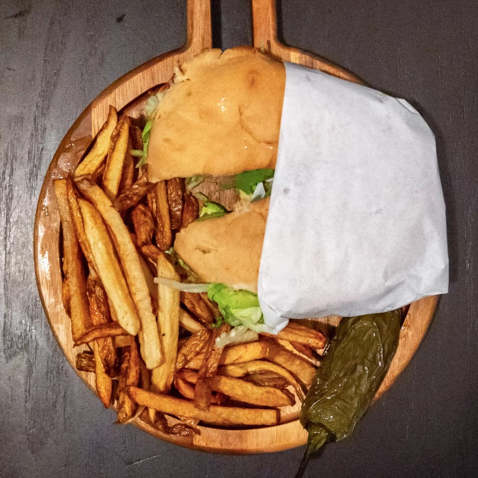 Two Mexican tortas wrapped in paper, with a side of fries and a grilled jalapeño.