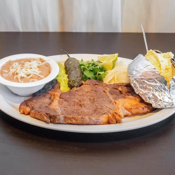 Mexican steak dinner with beans, grilled jalapeno, lime, cilantro, and a foil-wrapped baked potato.