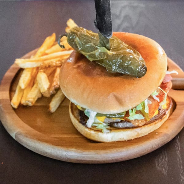 A Ciros Sea & Mexican Food burger with a grilled jalapeño on top, served with fries.