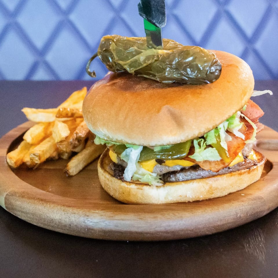 A Ciros Mexican burger with a grilled jalapeño on top, served with a side of fries.