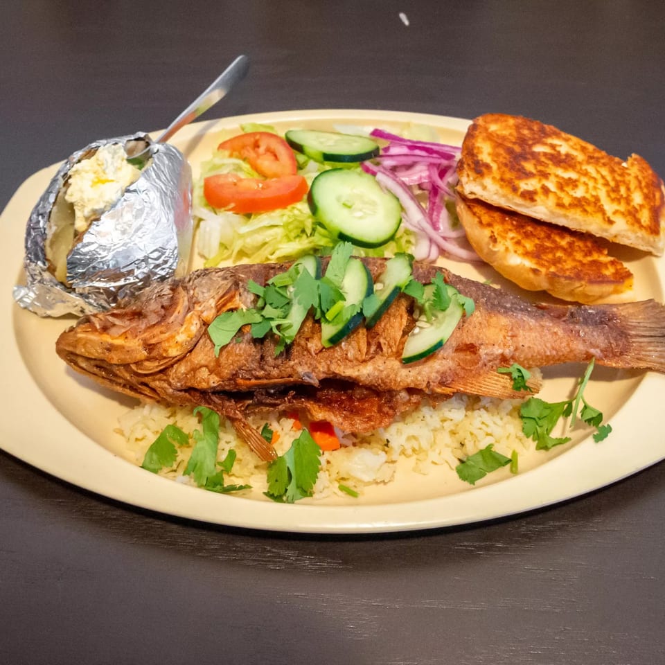 Whole fried fish with rice, salad, baked potato, and toasted bread on a yellow plate.