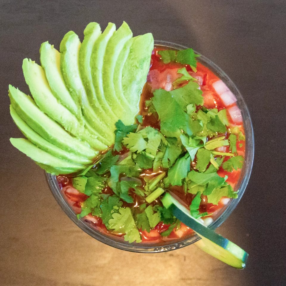 Overhead view of a vibrant Mexican seafood cocktail with avocado, cilantro, and cucumber.
