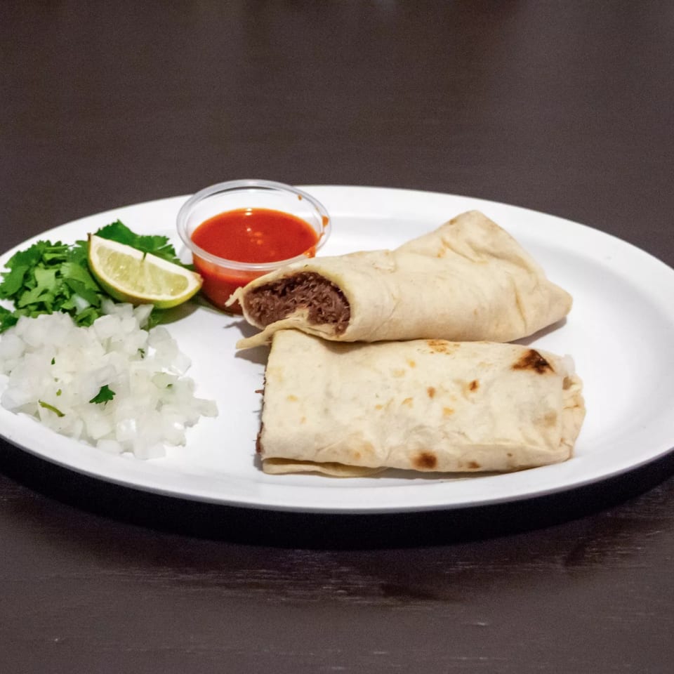 Two Ciros Mexican burritos with a side of chopped onions, cilantro, lime, and red sauce.