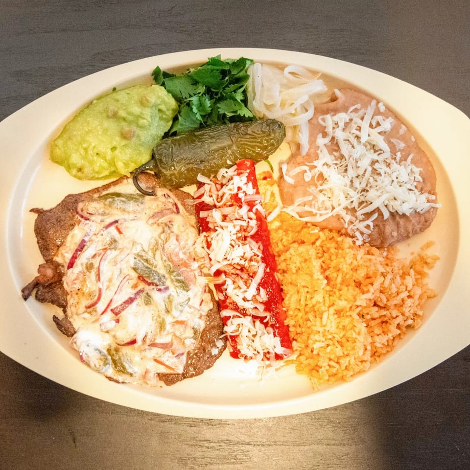 Mexican combination plate with steak, enchilada, rice, beans, guacamole, cilantro, and grilled pepper.